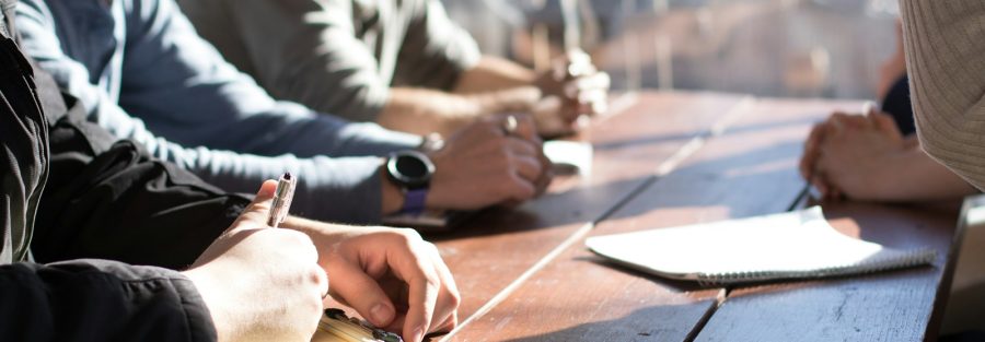 people sitting on chair in front of table while holding pens during daytime